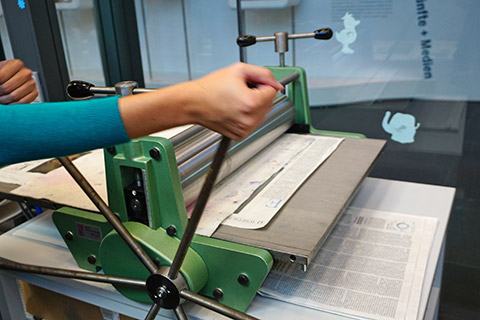 Eine Hand bedient das sechsarmige Speicherrad der Druckpresse