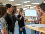 Eine Gruppe Benutzerinnen steht bei einer Benutzungseinführung im Lesesaal um einen Katalogbildschirm herum