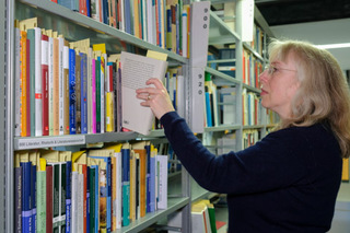 Eine Mitarbeiterin steht am Regal und sortiert Bücher nach den Sachgruppen der Deutschen Nationalbibliographie