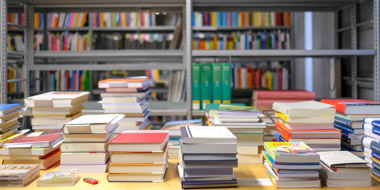 Sortiertisch mit Bücherstapeln, im Hintergrund teilweise gefüllte Bücherregale