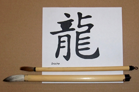 Two calligraphy brushes lying on a piece of white paper on which Chinese characters have been painted