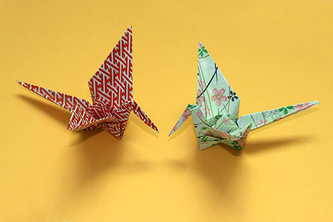 Origami cranes made of red and white patterned paper and green paper decorated with pink and blue blossoms
