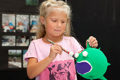 A girl painting a papier maché blowfish with green paint