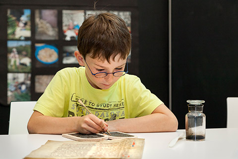 A child uses a stylus to carve letters into a wax tablet