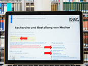 Opened laptop in front of a bookshelf, the screen shows the website of the online catalogue of the German National Library.