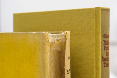 The badly damaged spine of a book in a before-and-after restoration comparison