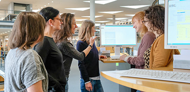 Eine Gruppe Benutzerinnen steht bei einer Benutzungseinführung im Lesesaal um einen Katalogbildschirm herum Eine Gruppe Benutzerinnen steht bei einer Benutzungseinführung im Lesesaal um einen Katalogbildschirm herum