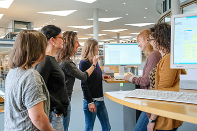 Eine Gruppe Benutzerinnen steht bei einer Benutzungseinführung im Lesesaal um einen Katalogbildschirm herum