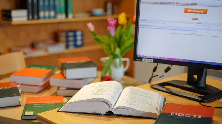 Gedruckte Ausgaben der Dewey Dezimalklassifikation an einem Arbeitsplatz mit dem Onlinetool Webdewey auf dem Computermonitor Gedruckte Ausgaben der Dewey Dezimalklassifikation an einem Arbeitsplatz mit dem Onlinetool Webdewey auf dem Computermonitor