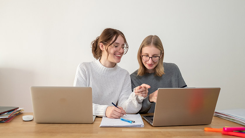 Zwei junge Frauen sitzen vor ihren Laptops.