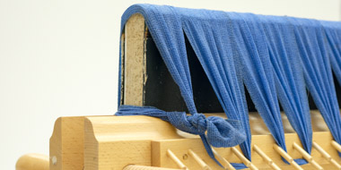Ein Buch ist in einer Holzpresse fixiert. Dabei wird der angesetzte Rücken des Buches durch eine elastische Binde niedergehalten