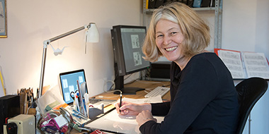 Eine Frau sitzt am Schreibtisch, schaut in die Kamera und hält einen Stift in der Hand. Eine Frau sitzt am Schreibtisch, schaut in die Kamera und hält einen Stift in der Hand.