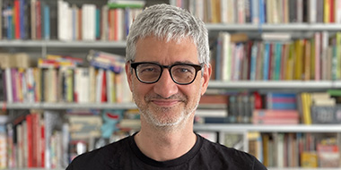 Ein Mann mit grauen Haaren und Brille steht vor einem Bücherregal Ein Mann mit grauen Haaren und Brille steht vor einem Bücherregal