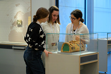 Drei Schülerinnen tauschen sich über die handgefertigte Tasche von Irma Lange aus. Die Tasche ist ein Exponat der Dauerausstellung des Deutschen Exilarchivs. 
