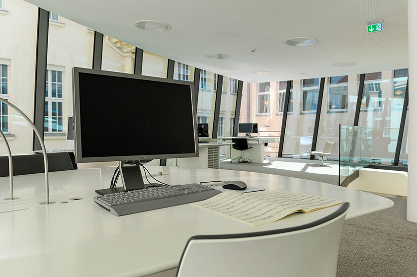 Arbeitsplatz mit Monitor und davor aufgeschlagenen Noten links neben der Treppe im Musiklesesaal  Arbeitsplatz mit Monitor und davor aufgeschlagenen Noten links neben der Treppe im Musiklesesaal