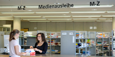 A staff member at the issues desk scanning books to be borrowed by a user