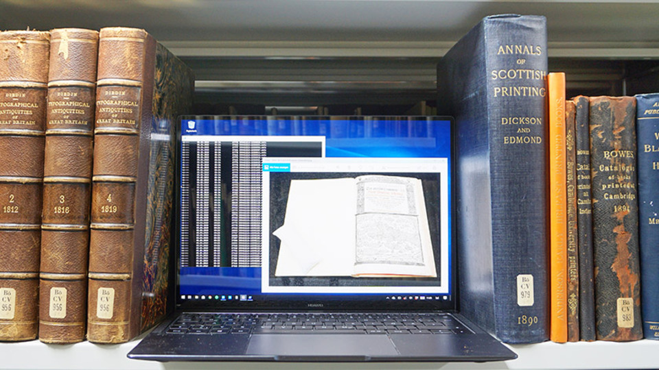 Switched-on laptop and books on the shelves of a library Switched-on laptop and books on the shelves of a library