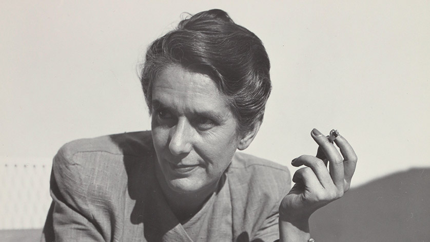 The black-and-white photo shows Erika Mann at the age of 43. She is looking toward the right and holding a cigarette between the fingers of her left hand.