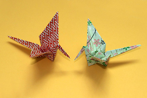 Origami cranes made of red and white patterned paper and green paper decorated with pink and blue blossoms Origami cranes made of red and white patterned paper and green paper decorated with pink and blue blossoms