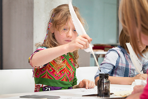 A girl dips a quill pen into an ink pot A girl dips a quill pen into an ink pot