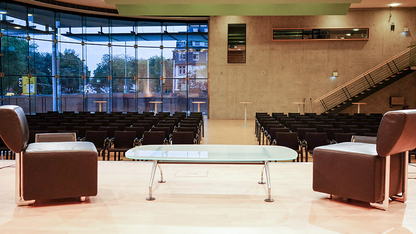 View from the stage of the lecture hall at the German National Library in Frankfurt am Main, with rows of seats in the auditorium and two armchairs and a glass table on stage. View from the stage of the lecture hall at the German National Library in Frankfurt am Main, with rows of seats in the auditorium and two armchairs and a glass table on stage.
