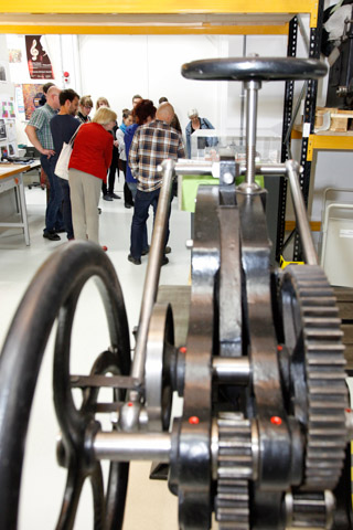 Besuchergruppe im Schaudepot des Deutschen Buch- und Schriftmuseums, im Vordergrund Zahnräder und Kurbeln einer Druckmaschine Besuchergruppe im Schaudepot des Deutschen Buch- und Schriftmuseums, im Vordergrund Zahnräder und Kurbeln einer Druckmaschine