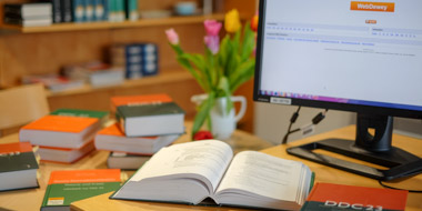 Printed editions of the Dewey Decimal Classification system at a workstation with the Webdewey online tool on the computer screen Printed editions of the Dewey Decimal Classification system at a workstation with the Webdewey online tool on the computer screen