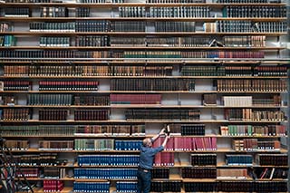 Book-shelf full of books, with a man standing before it and returning a book.
