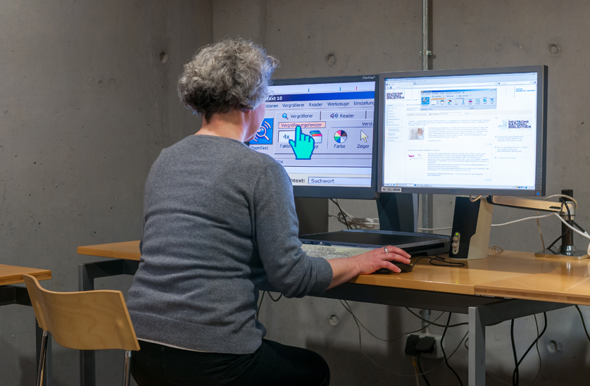 You can see a person sitting in front of two monitors. On the left-hand monitor, everything is shown in greatly enlarged form. You can see a person sitting in front of two monitors. On the left-hand monitor, everything is shown in greatly enlarged form.