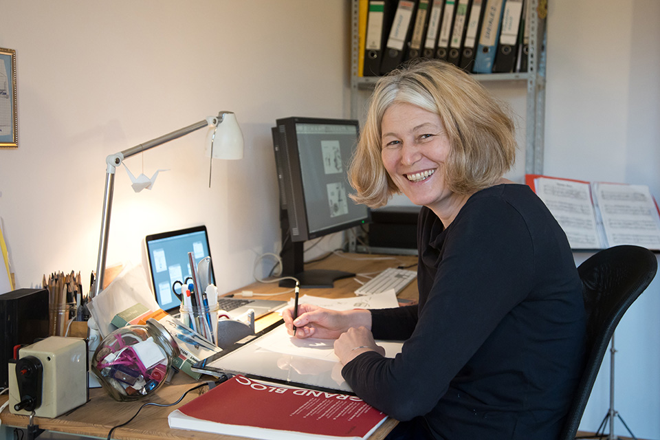 A woman is sitting at a desk, looking at the camera and holding a pen in her hand. A woman is sitting at a desk, looking at the camera and holding a pen in her hand.