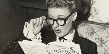 Photo of a young woman wearing glasses and gazing at a book (on Einstein’s theory of relativity) with a look of surprise on her face Photo of a young woman wearing glasses and gazing at a book (on Einstein’s theory of relativity) with a look of surprise on her face