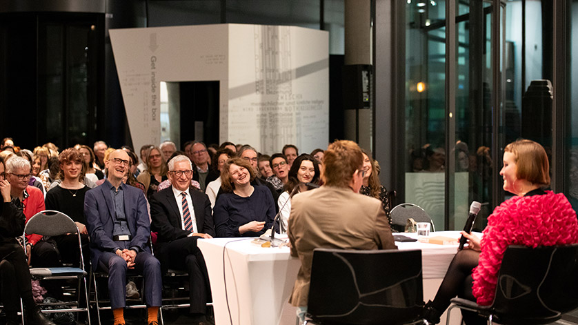Caroline Wahl in conversation with Andrea Reidt on the podium in front of an audience in the hall.  Caroline Wahl in conversation with Andrea Reidt on the podium in front of an audience in the hall.